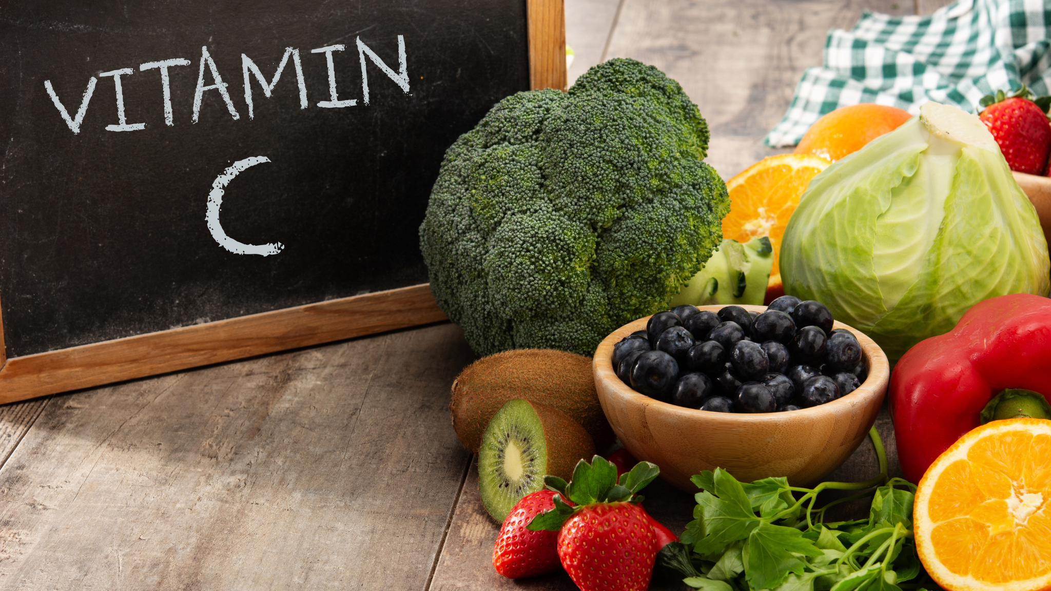 a small blackboard on top of a table with Vitamin C written in chalk on it with a lot of vitamin C rich fruits and vegetables showing for the Hope Health and Wellness Advocacy blog Vitamin C - Everything You Need and Want To Know Especially During Respiratory Virus Season